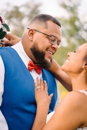 Joyful wedding couple embracing outdoors, with the bride's hand resting on her groom's chest.