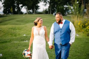 Wedding couple shares a joyful moment while walking on lush green grounds.