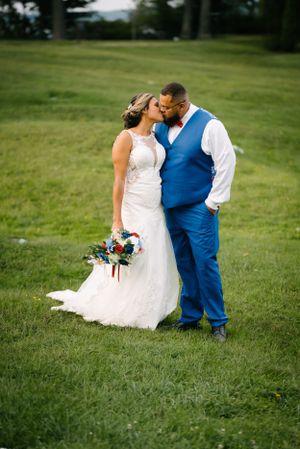 Couple shares romantic moment in wedding attire against green outdoor backdrop.