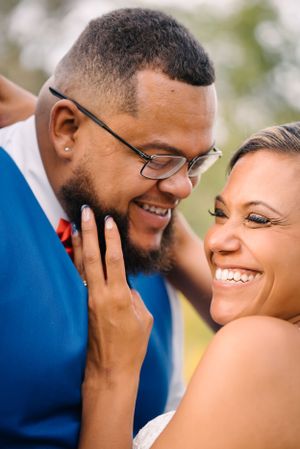A tender moment between newlyweds as they share a loving smile, with the groom in a blue suit and red bowtie.