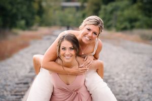 Two attendants in formal attire share a playful piggyback moment on train tracks.