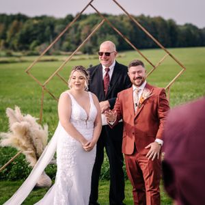 Wedding ceremony under a geometric copper arch with rustic outdoor decor.