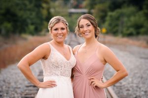 Two wedding attendants in blush pink and white dresses pose together on train tracks.