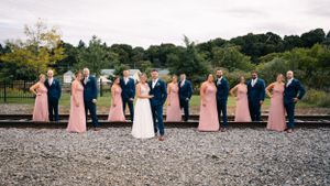 Wedding party lines up on railroad tracks wearing pink dresses and navy suits.