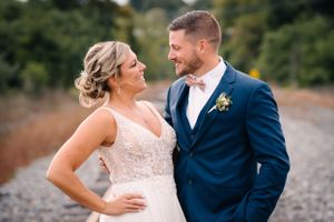 Couple in wedding attire shares romantic moment on rustic train tracks.
