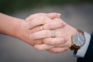 Close-up of newlywed hands showing wedding rings with a watch visible in frame.