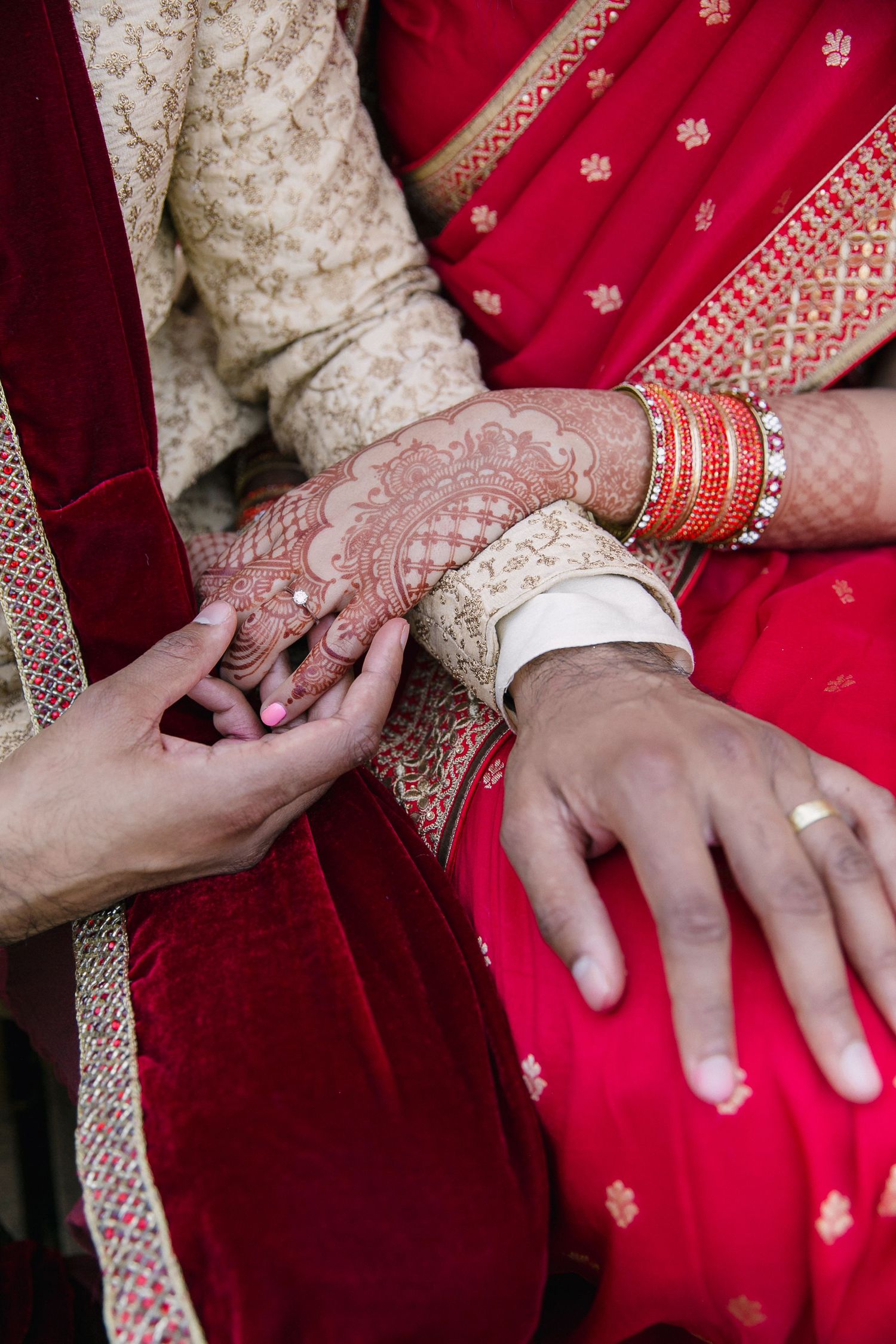 A couple holding hands showing their traditional Hindu wedding attire and the bride's henna hand art.