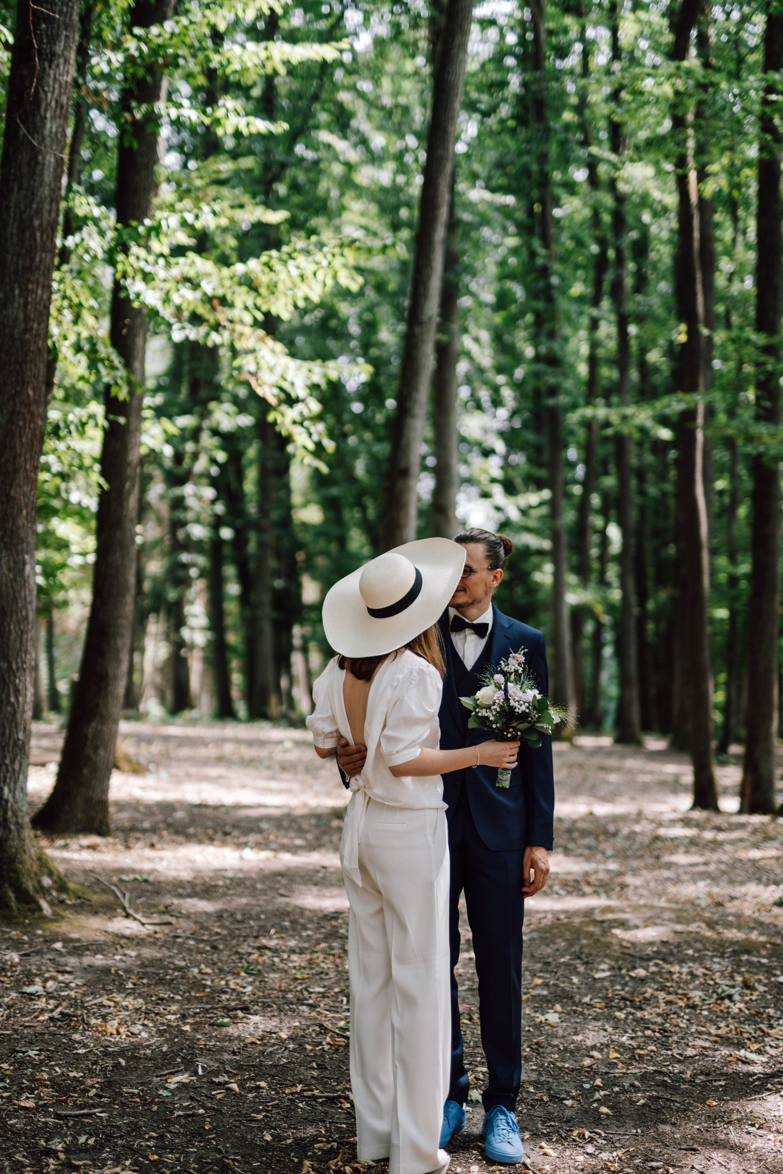 Couple in wedding attire sharing drinks in a wooded setting.