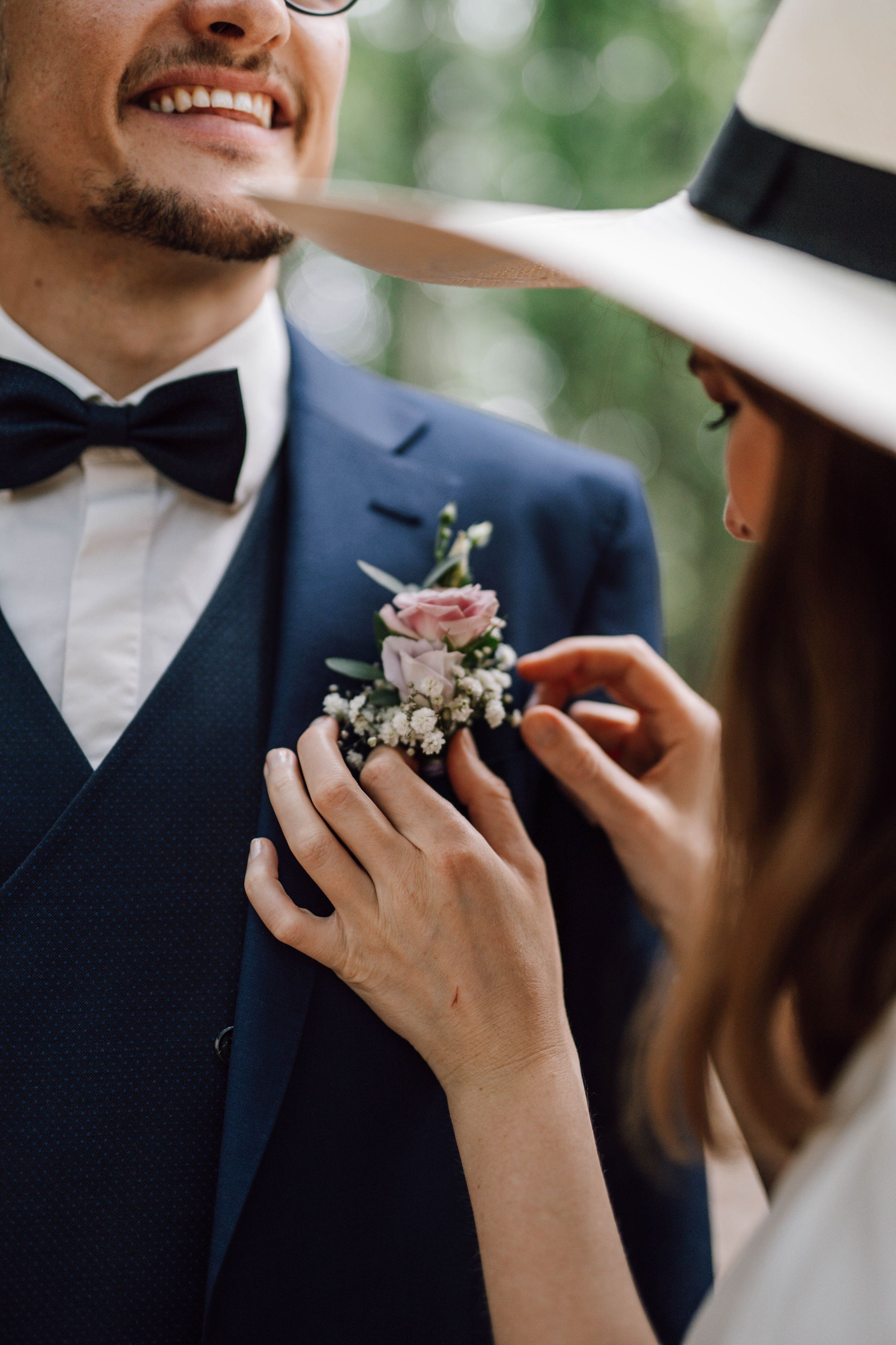 Close-up of hands pinning a boutonniere onto a navy blue suit jacket.