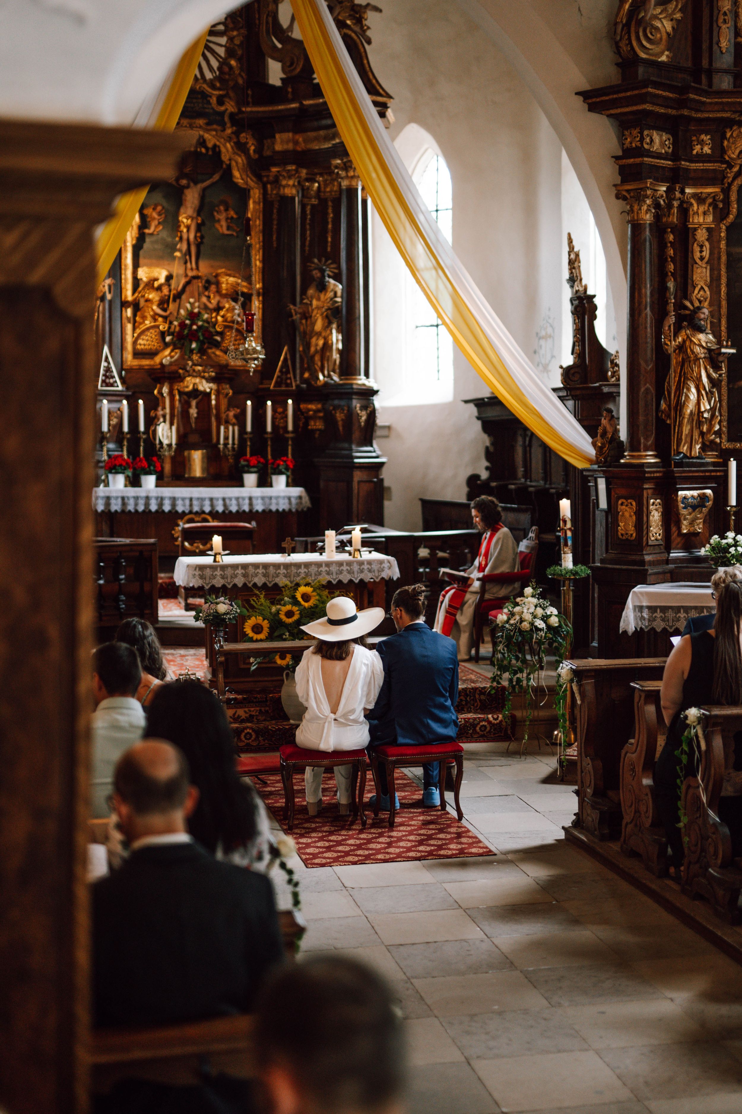 Interior of an ornate church with golden altars and traditional decorations during a wedding ceremony.