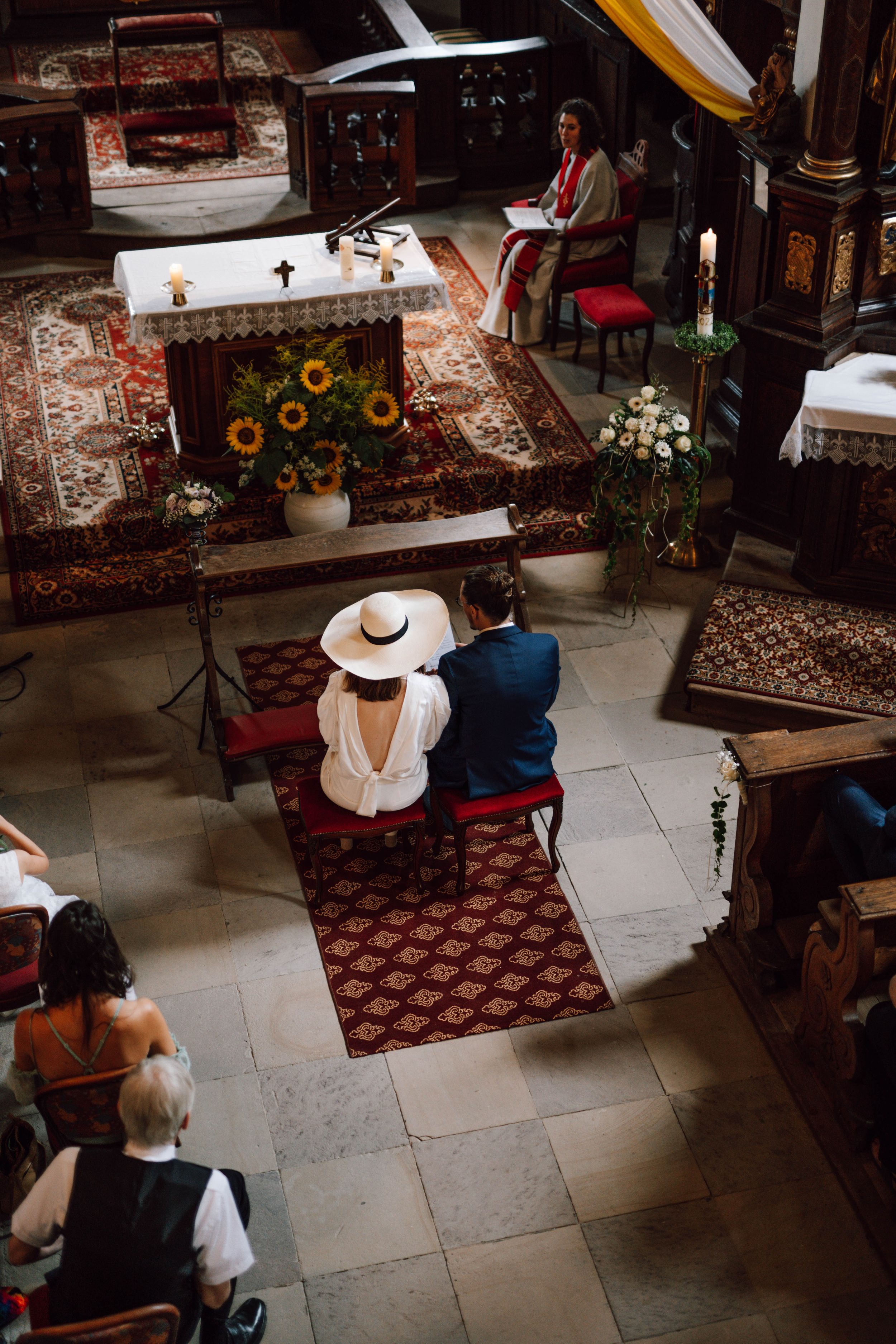 Overhead view of a church interior with sunflowers decorating the altar and people seated in traditional attire.