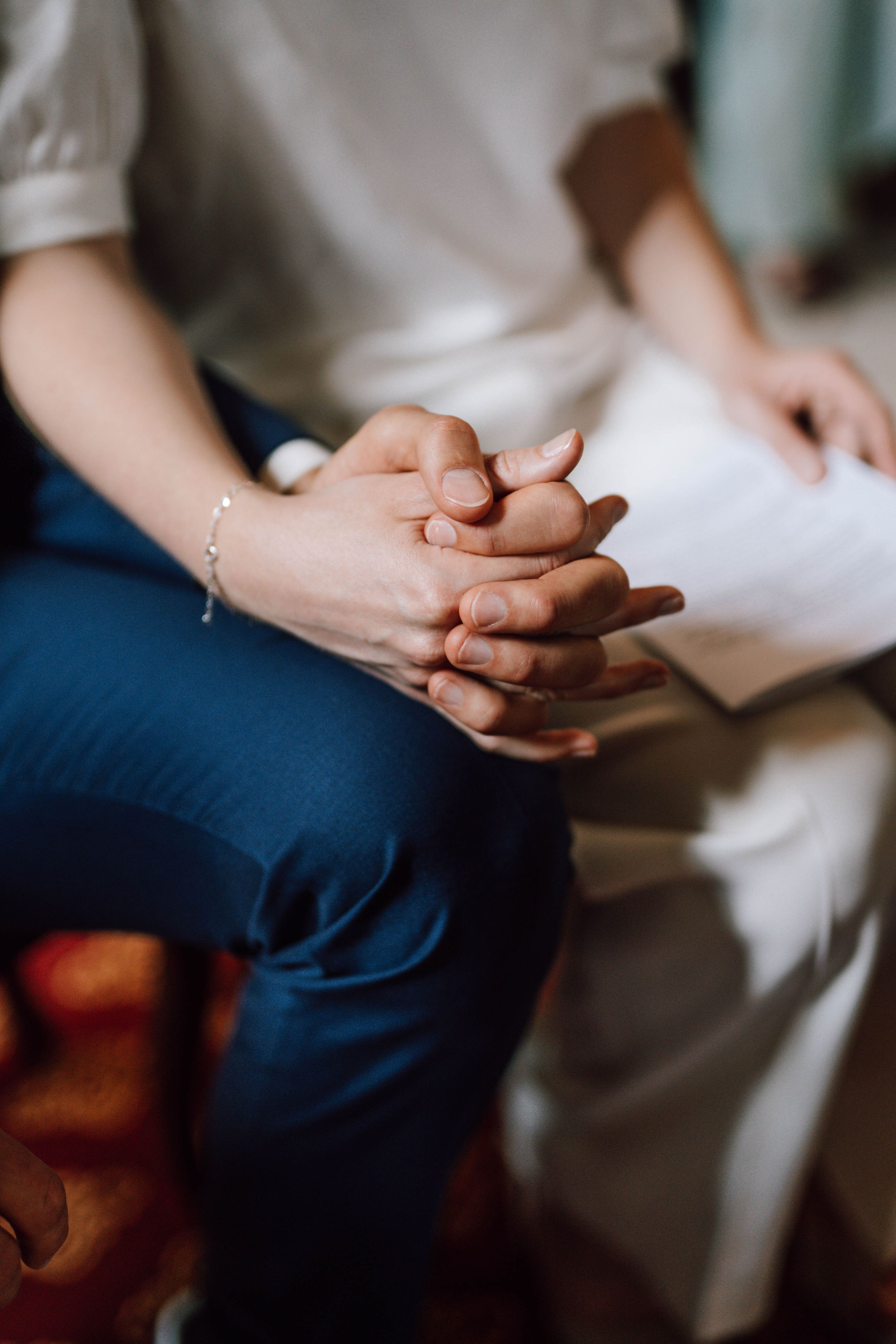 Close-up of clasped hands resting on blue pants against a white background.