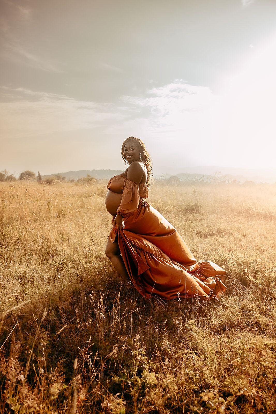 An expectant mother walks through a field while playing with her dress during her maternity session in Charlottesville.