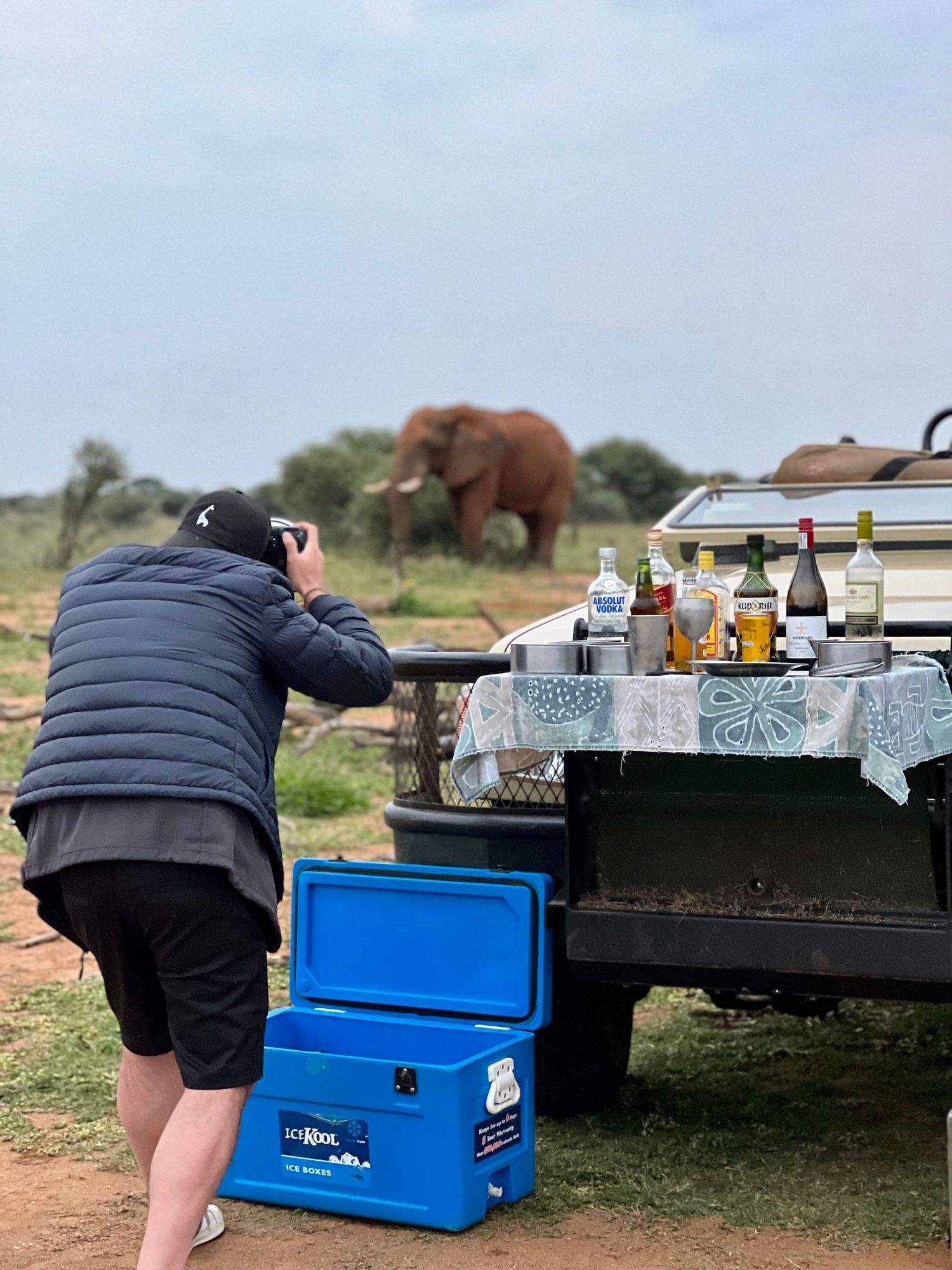 Safari sundowner setup with drinks and coolers on outdoor tables in African wilderness.