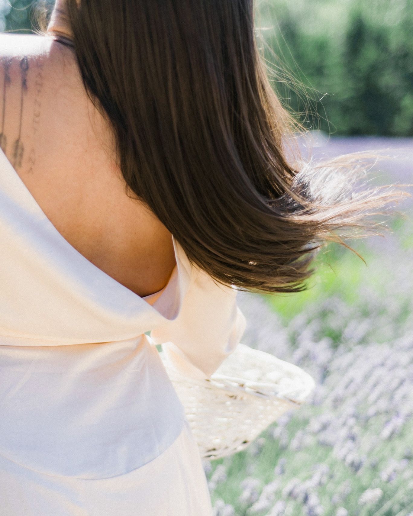 Close-up of flowing dark hair and white fabric against blurred natural background.