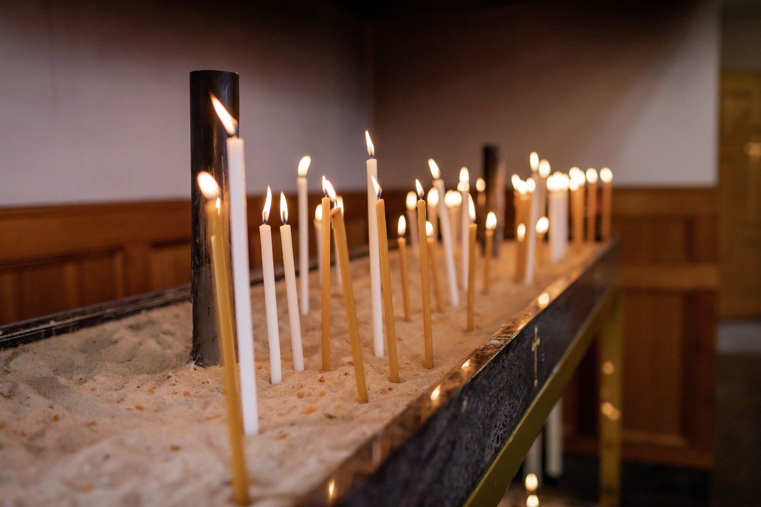 Row of lit white candles on dark wooden surface in church.