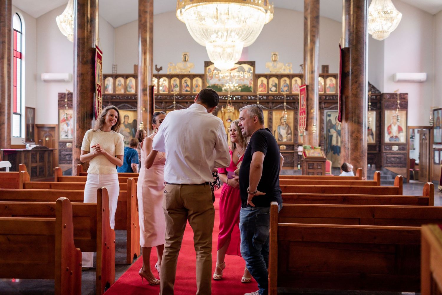 People gathering inside a church with crystal chandeliers and ornate wooden details.