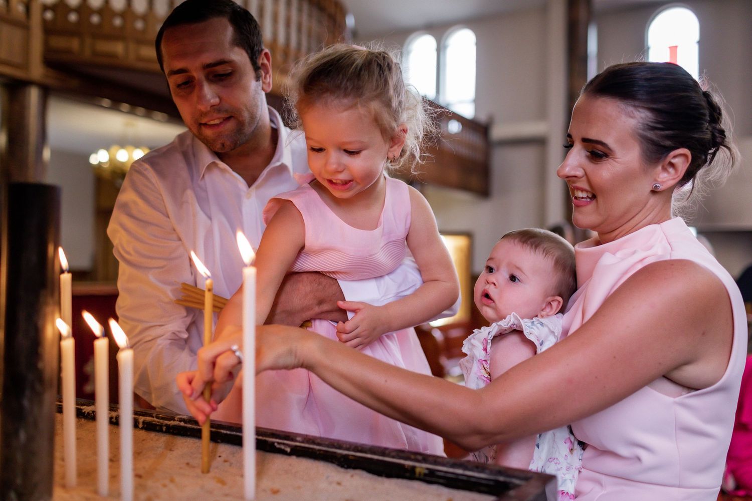 Family lighting candles together during church ceremony.