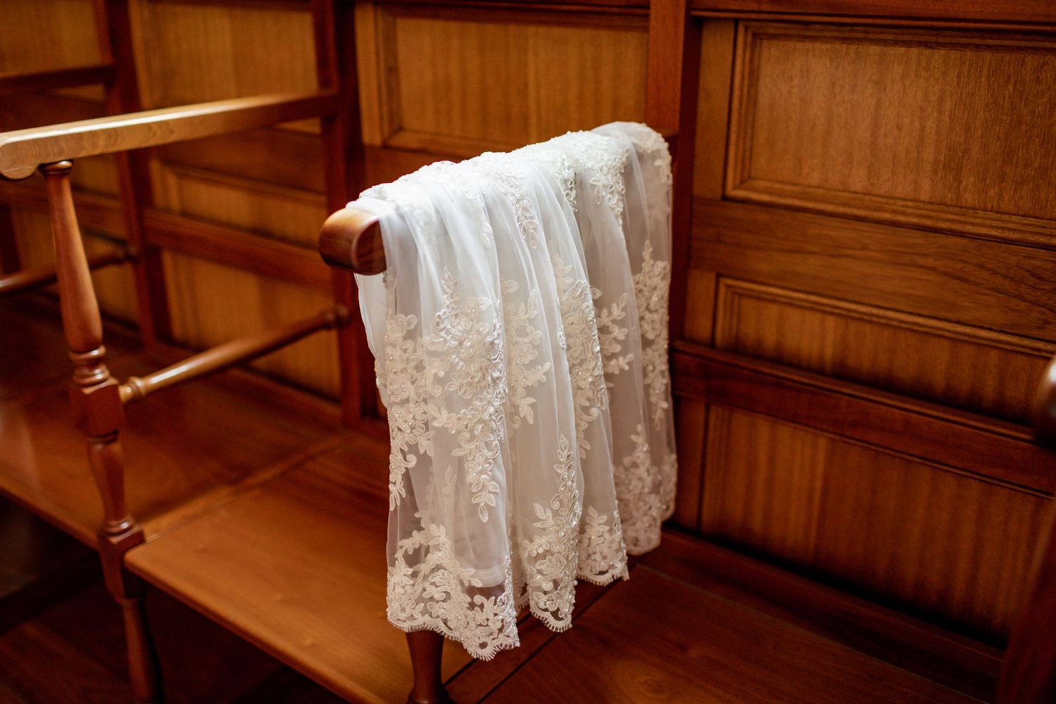 Delicate white lace baptismal gown draped over wooden church pew.
