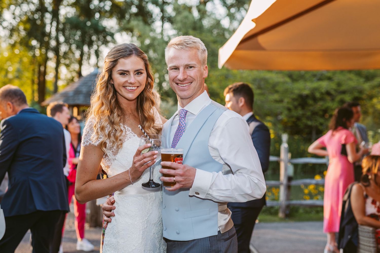 Couple sharing drinks at an outdoor wedding reception during golden hour.