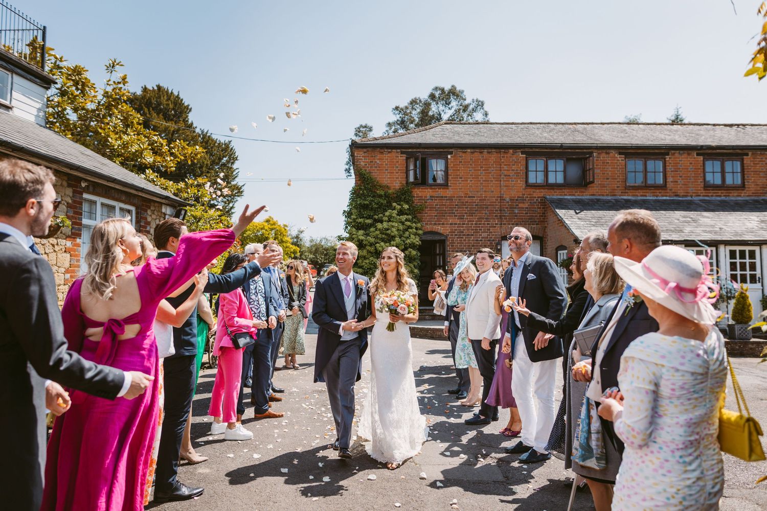 Wedding guests throwing confetti at a celebration outside a brick building on a sunny day.