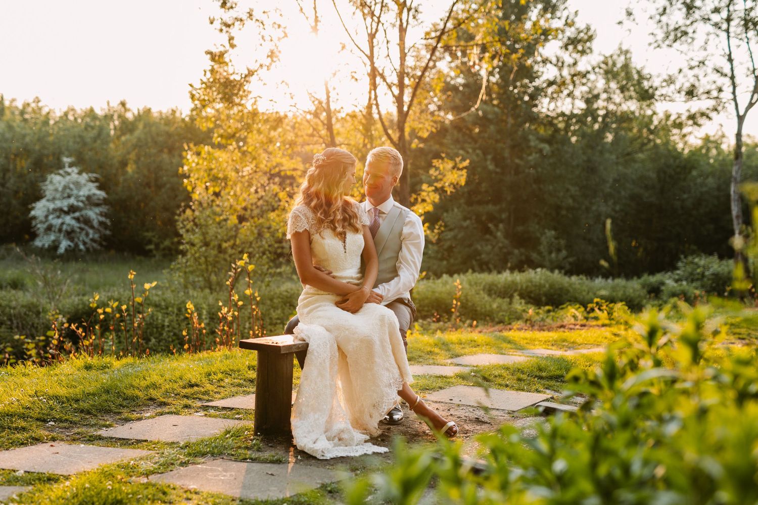 Wedding couple sitting together on stone steps in a garden at sunset.