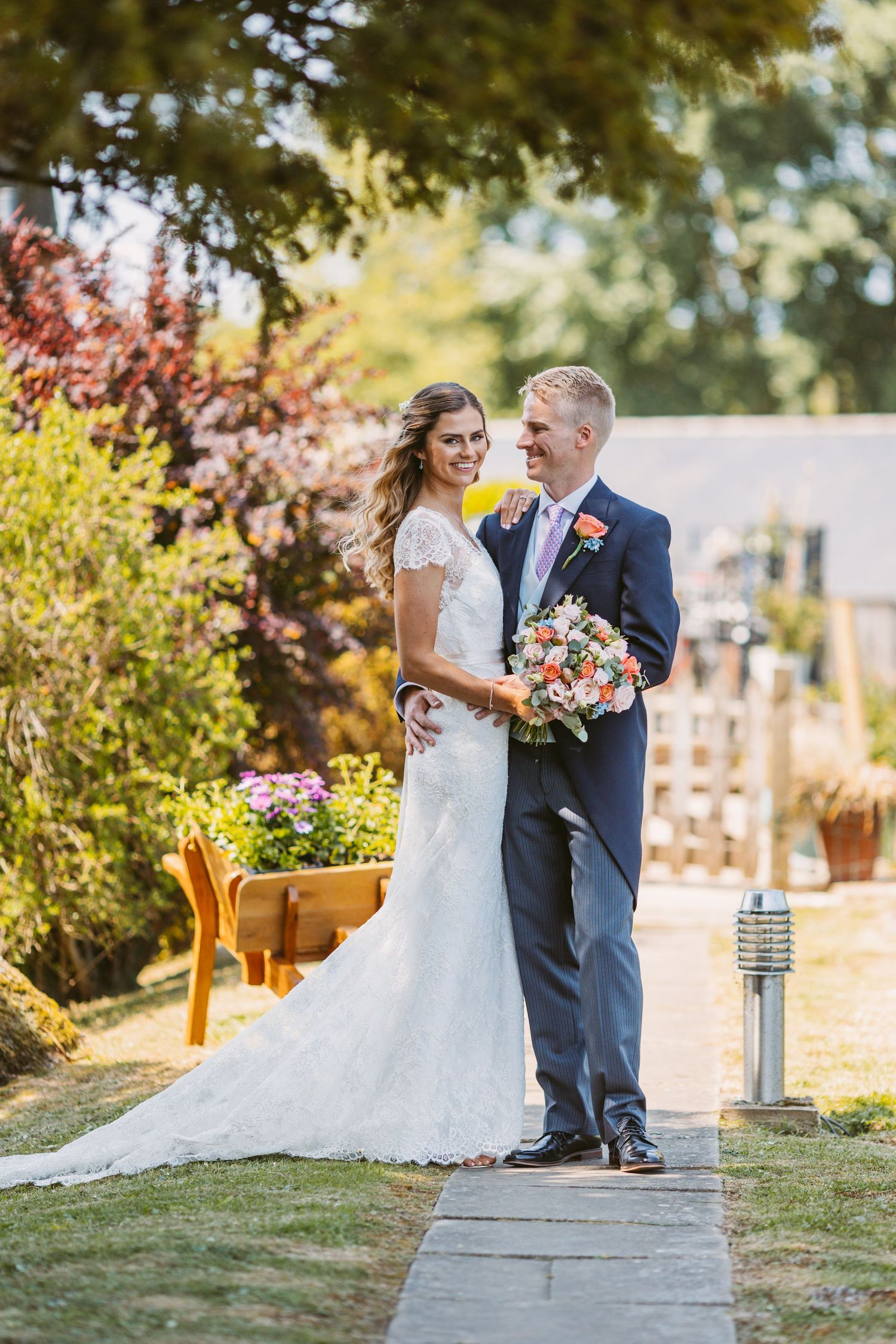 A wedding couple standing on a garden path surrounded by colorful autumn foliage.