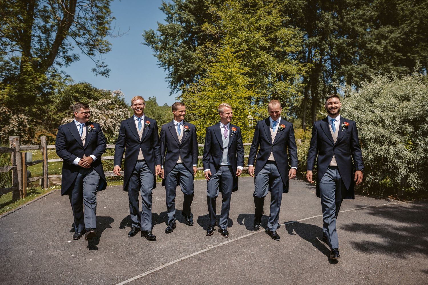 Groomsmen in matching navy suits walking together outdoors in a park.