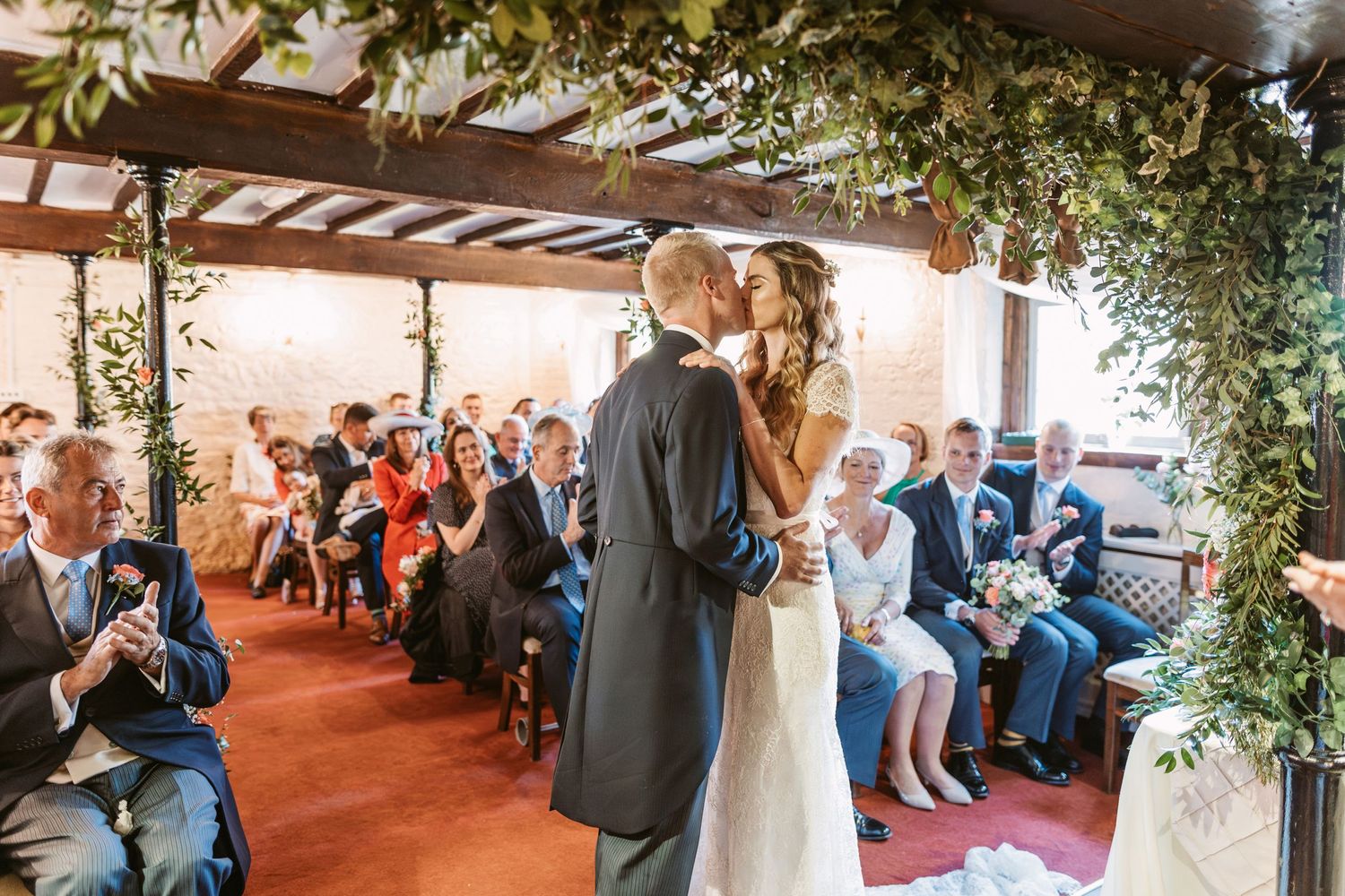 Indoor wedding ceremony with floral archway and seated guests watching the couple.