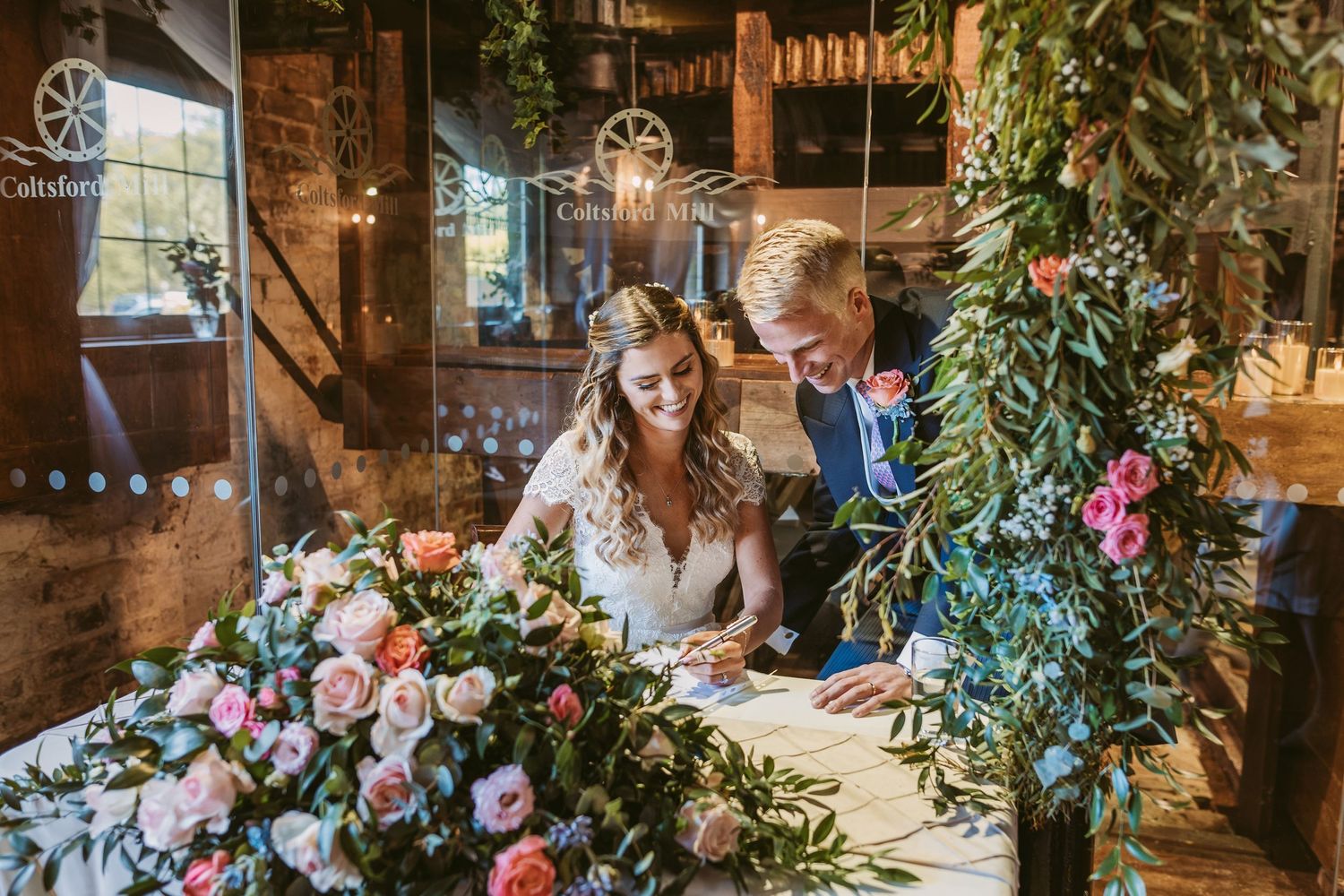 Couple signing wedding documents at a decorated rustic table with floral arrangements.
