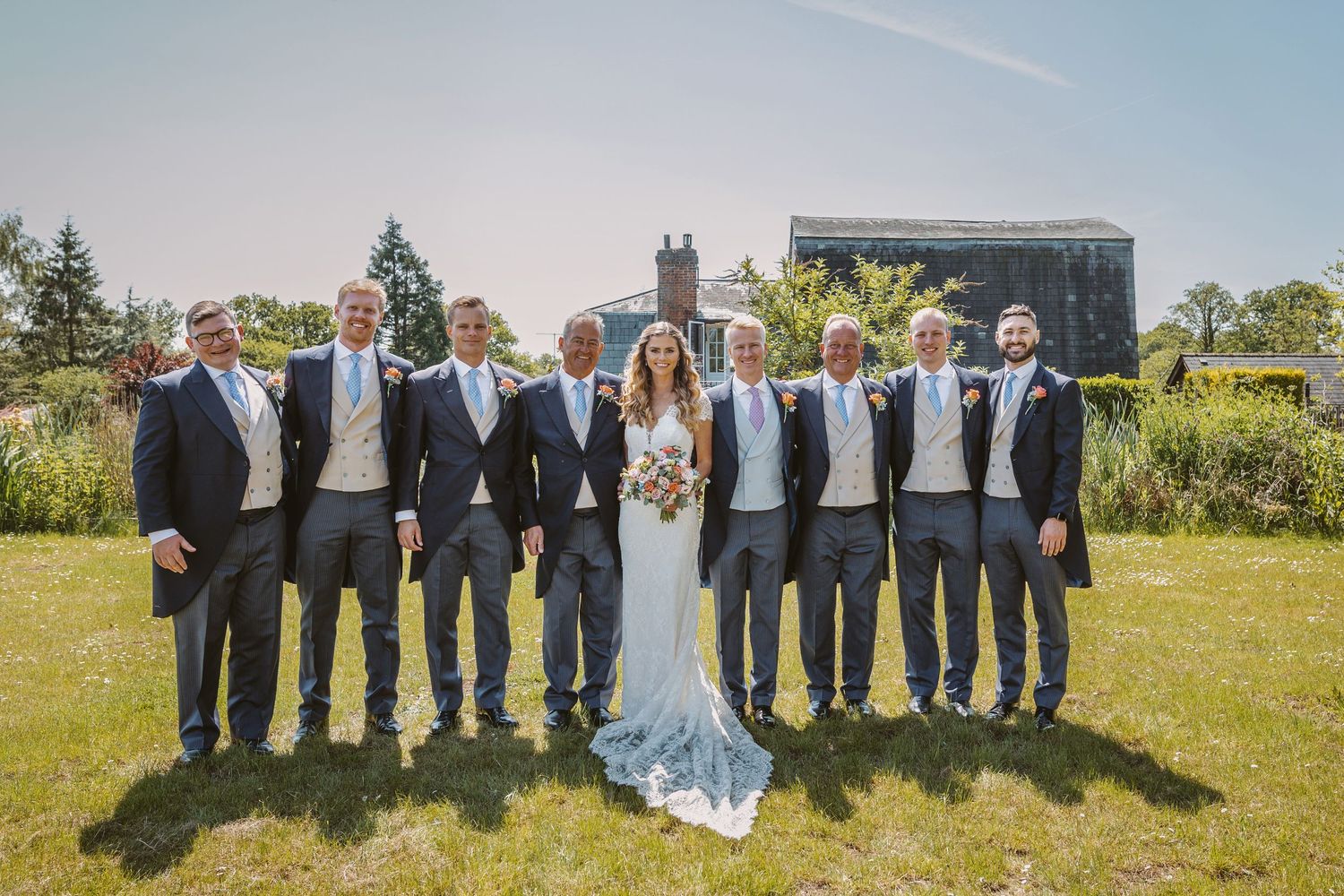 Wedding party in gray and white attire posing together on a sunny lawn.
