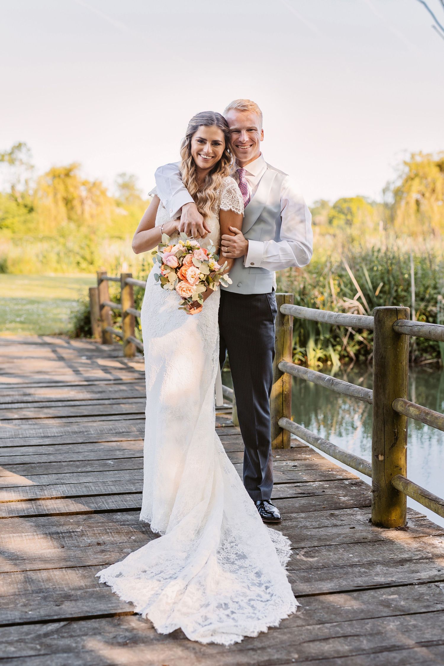 Newlyweds share an intimate moment on a wooden boardwalk over water in a beautiful outdoor setting.