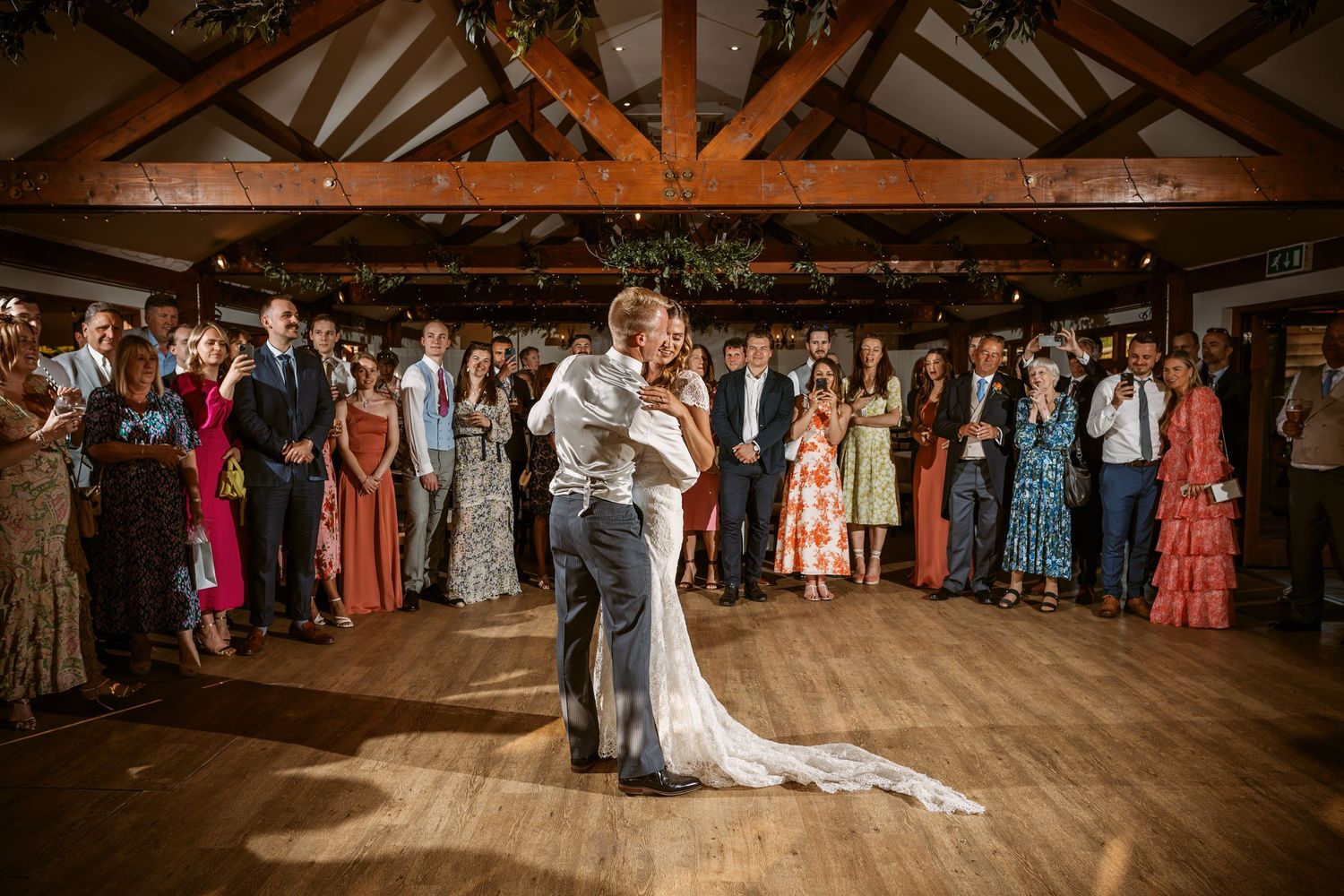 Wedding couple shares an intimate dance moment in a rustic reception venue with guests watching.