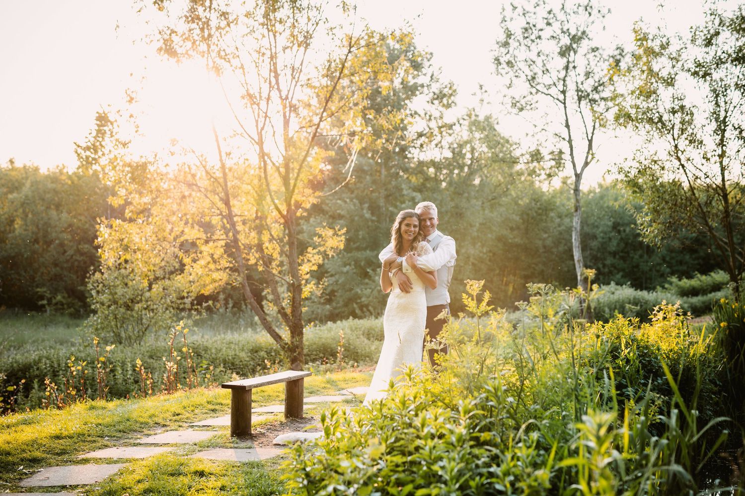 A romantic sunset wedding portrait on a nature path surrounded by wildflowers and golden light.