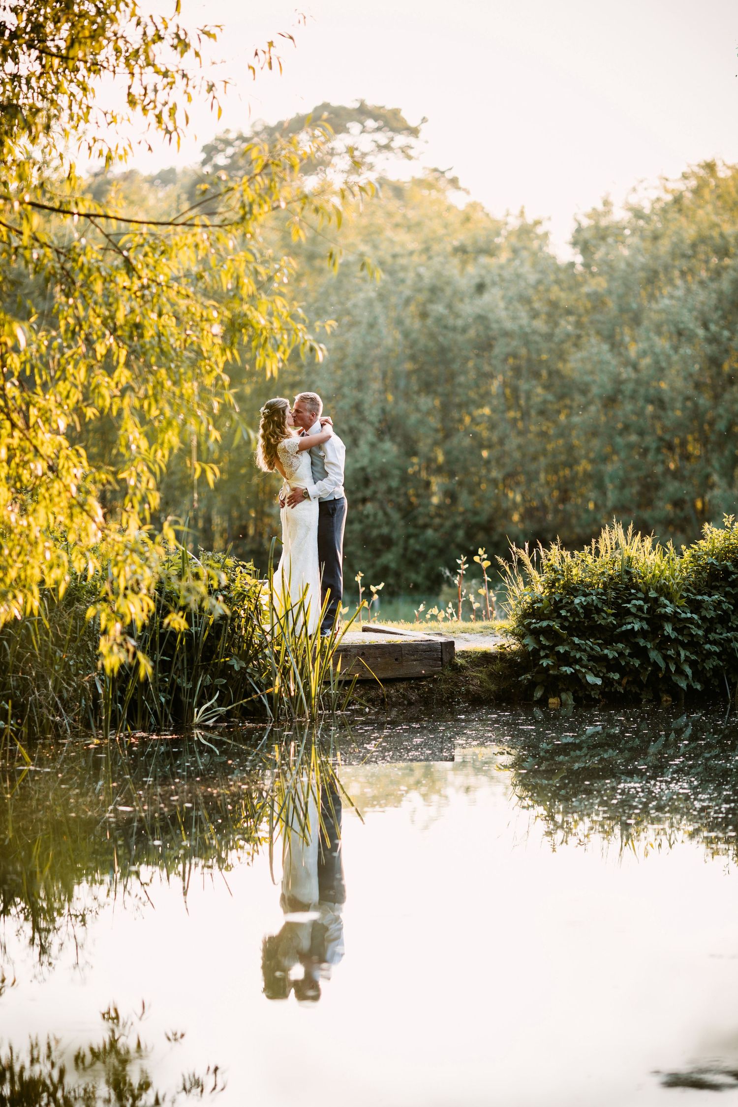 Romantic couple embraces by a reflective pond surrounded by golden autumn foliage at sunset.