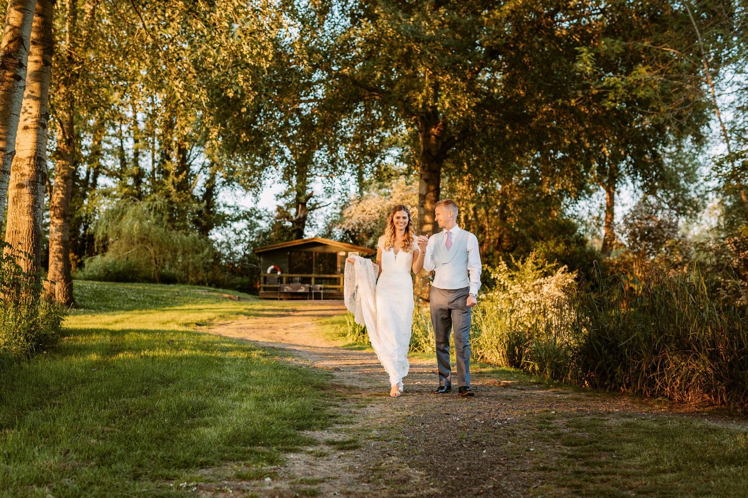 Happy couple walks along a garden path surrounded by lush trees on a sunny day.
