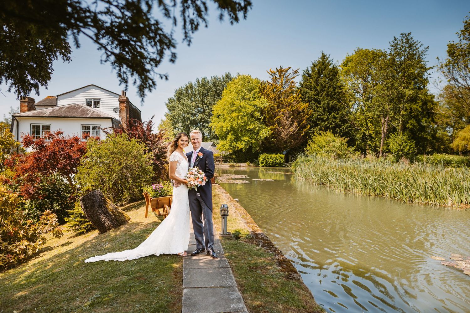 A romantic wedding portrait on a wooden dock overlooking a serene pond with autumn trees.