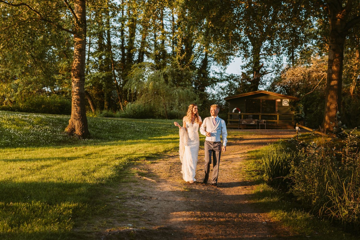 Couple walking hand in hand on a tree-lined path in golden evening light.