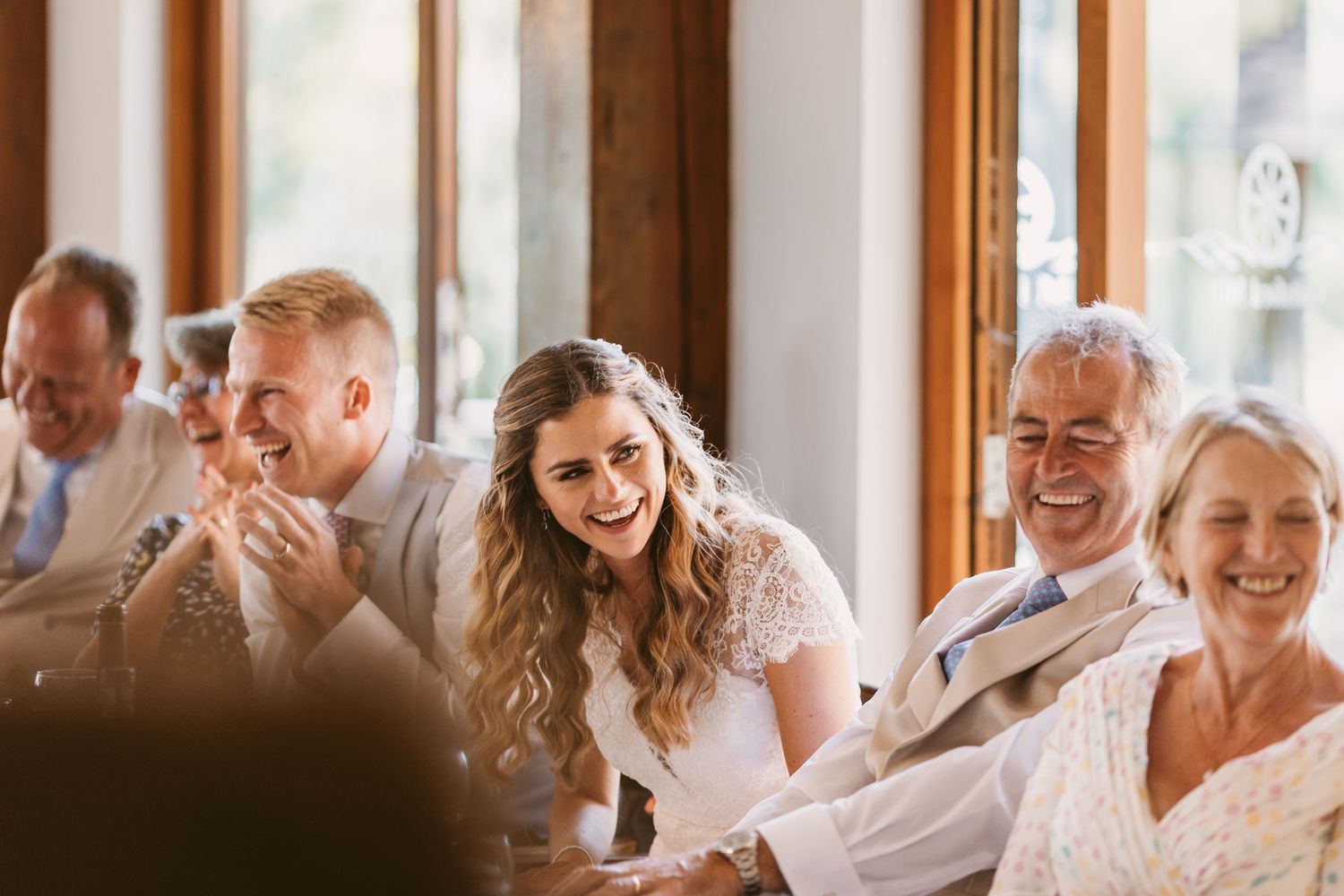 Wedding reception guests laughing and enjoying celebrations in a sunlit venue.