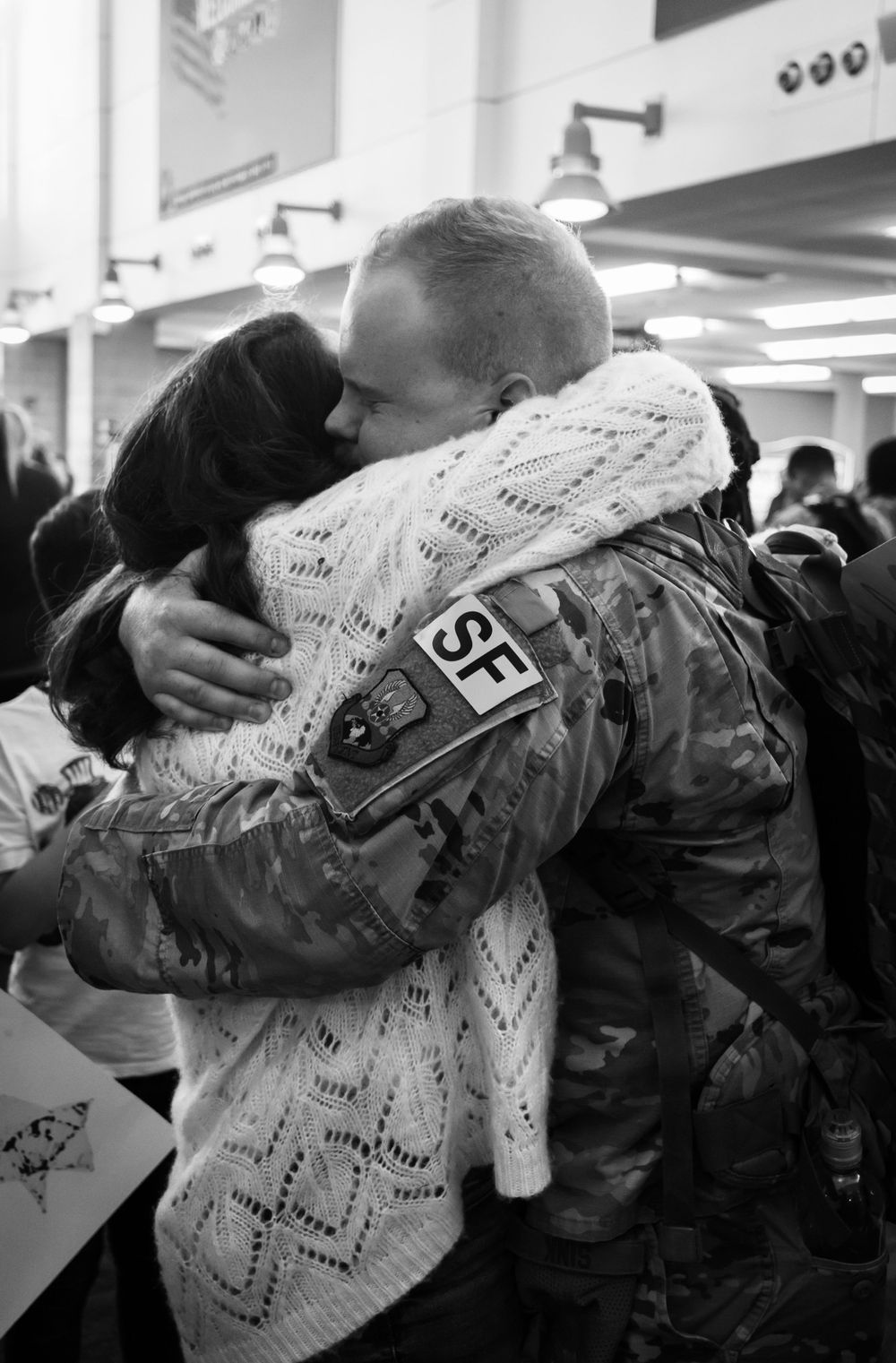 Black and white photo of emotional military homecoming hug between soldier in camo and loved one.