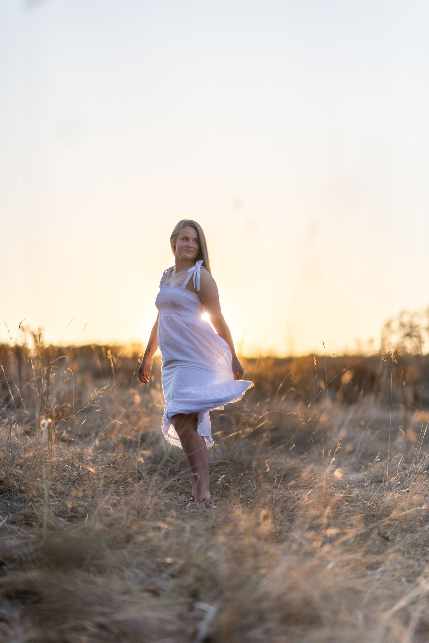 model in golden hour. golden field with sun behind her.