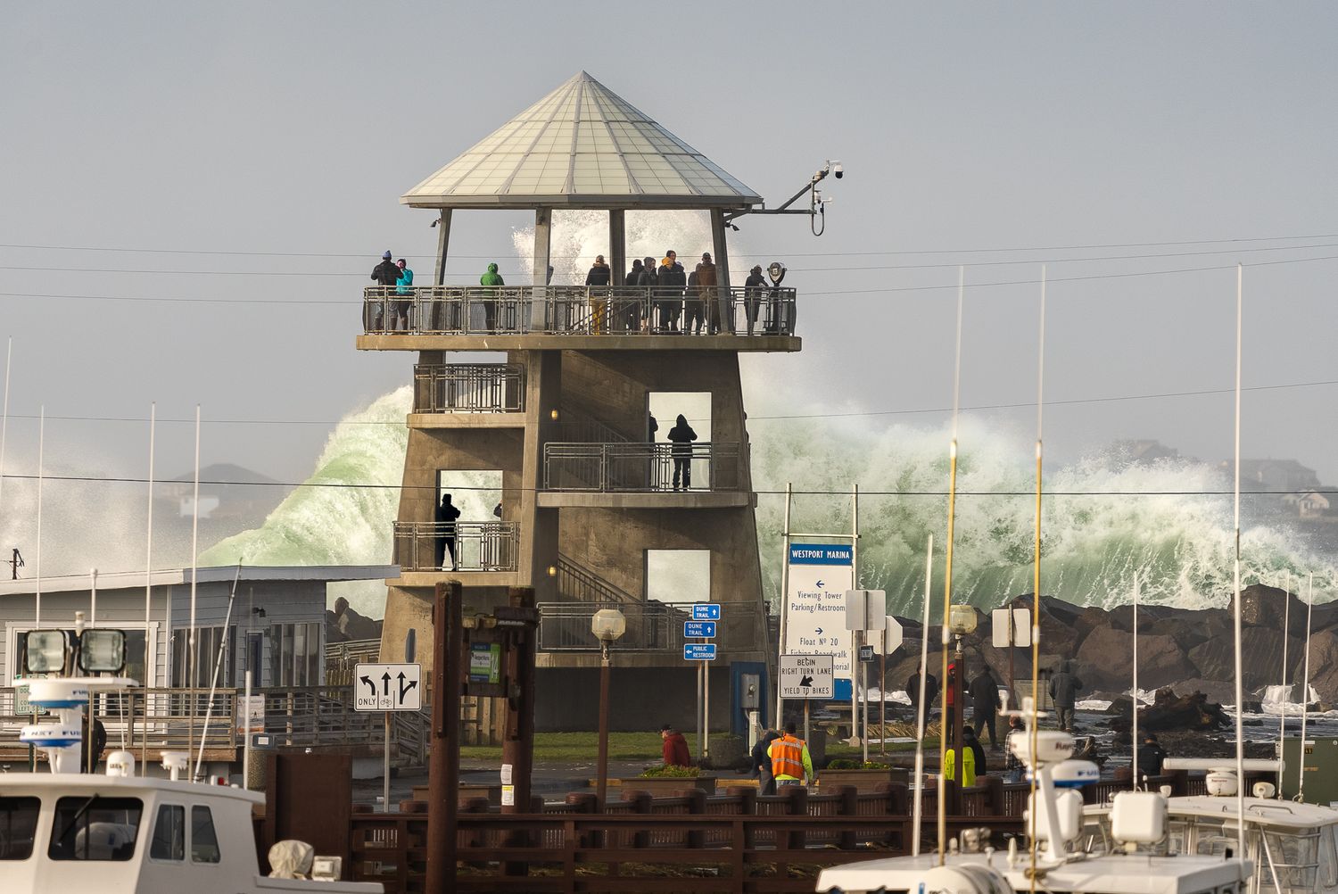 Observation tower filled with onlookers as massive waves crash against harbor wall.