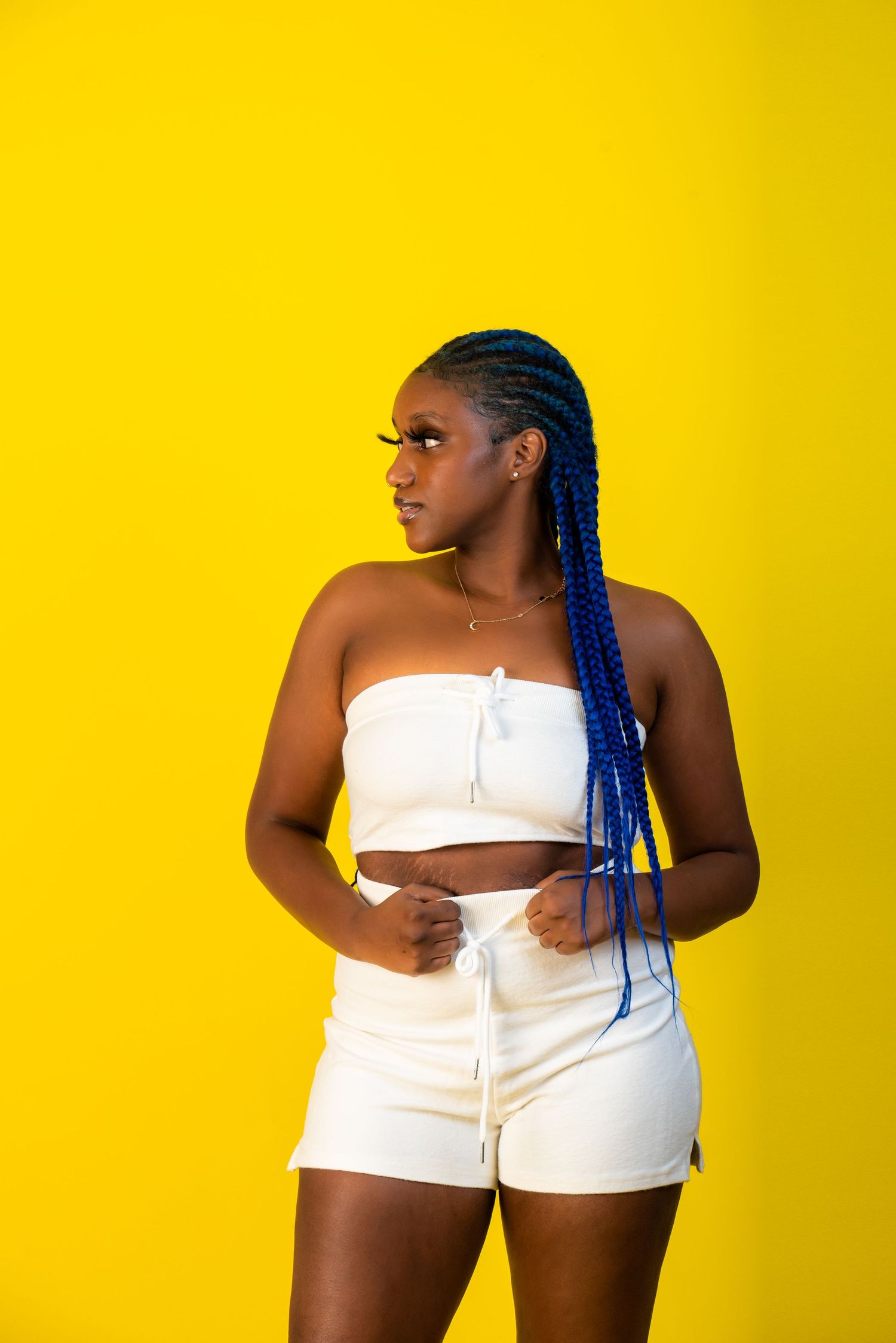 Fashion poses in white summer outfit against bright yellow studio backdrop.