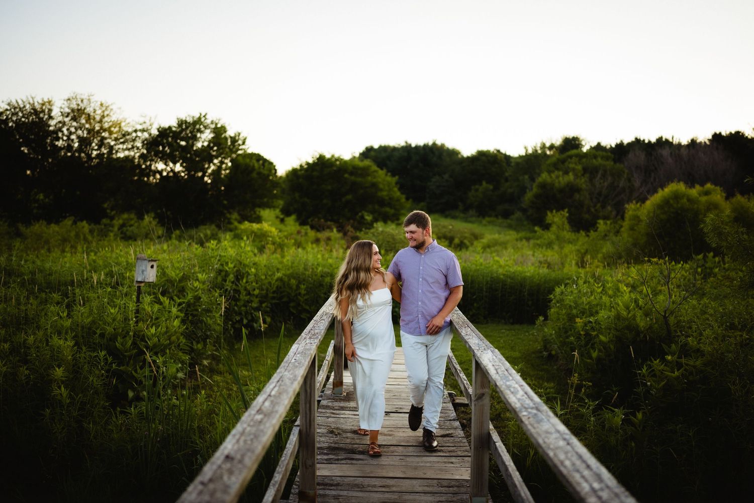A couple walking together on a wooden boardwalk through a natural wetland area.