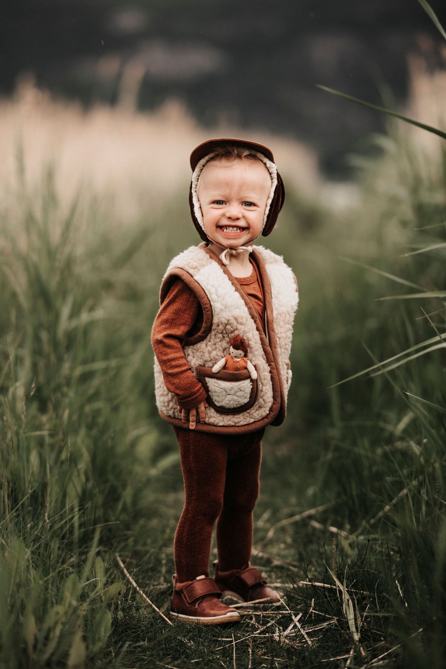 smilende gutt med dokke i ullvest ute i gresset babyfotografering