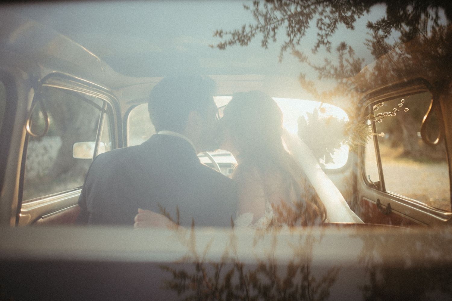 Silhouettes of a couple sharing an intimate moment in a vintage car at sunset.