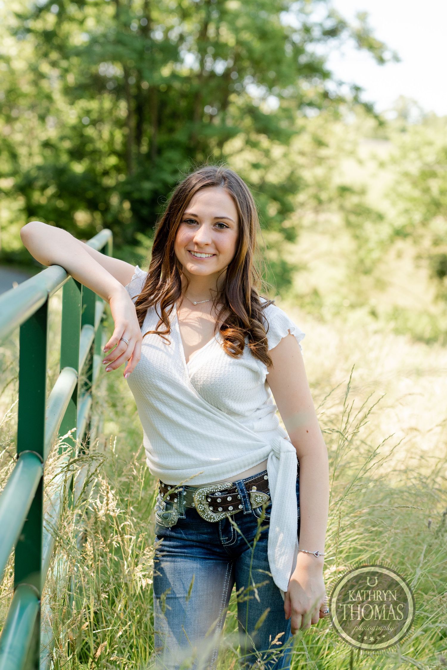 A summer portrait by a green railing in a white top and embellished belt.