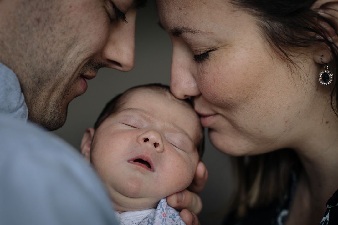 A tender family moment with a sleeping infant being embraced by parents.
