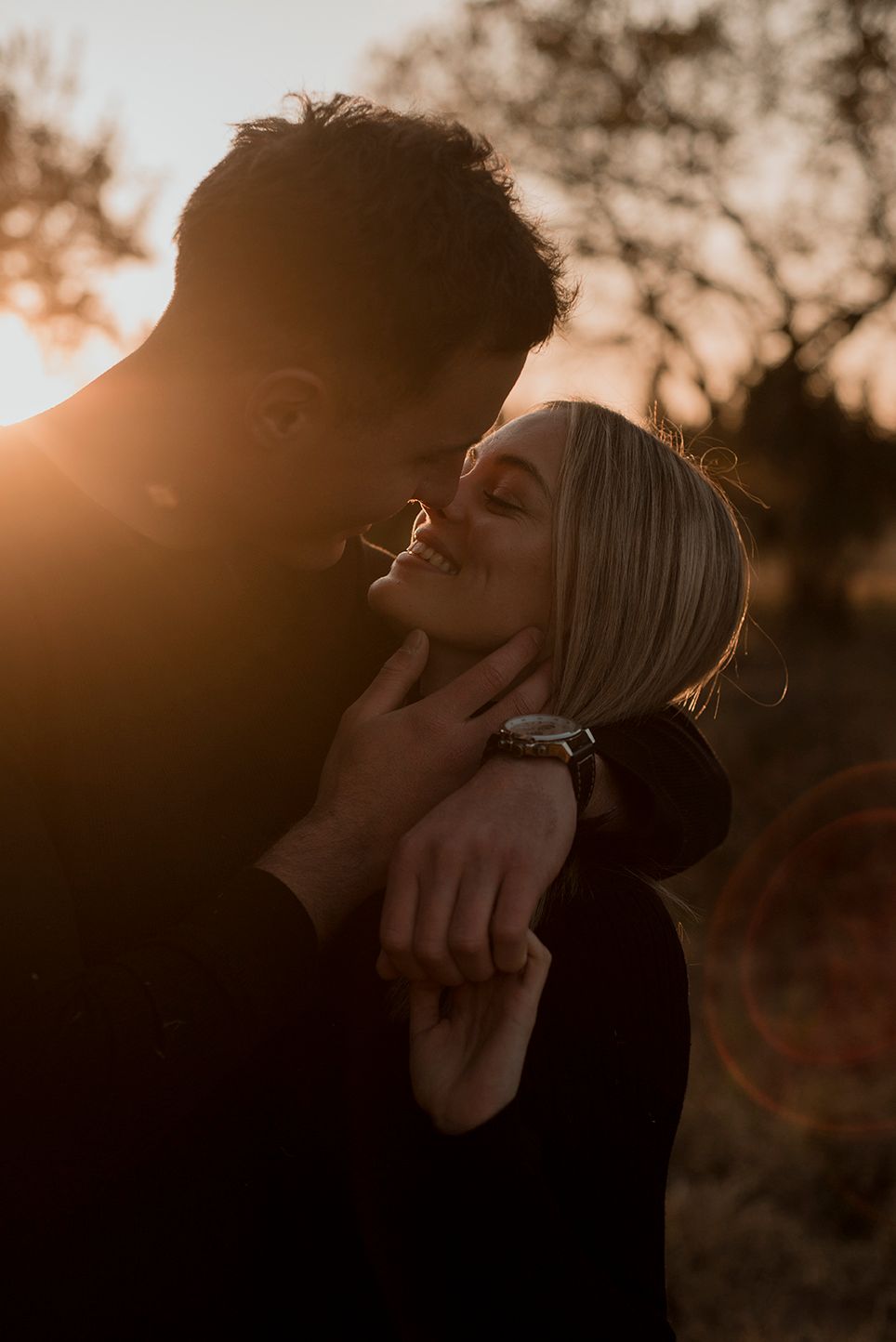 Couple embracing during golden hour with warm sunset light in the background.