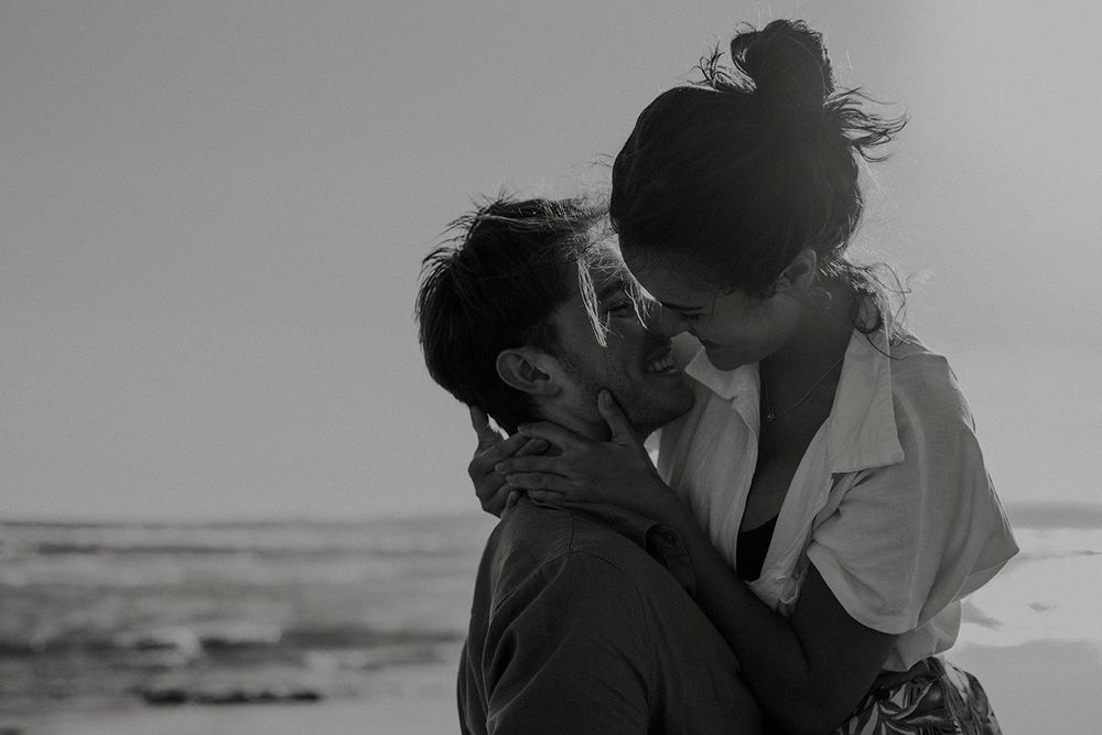Couple embracing during golden hour with warm sunset light in the background on the beach.